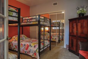 Une chambre avec un lit superposé, une literie à motifs floraux, une armoire en bois et un miroir au mur.