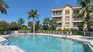 A swimming pool with lounge chairs and palm trees, surrounded by a multi-story building. - Gorgeous 3B/2B Island Condo At Bella Lago, Pool, Walk To Beach (Fort Myers Beach)