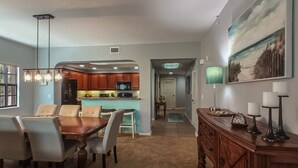 Un comedor con mesa y sillas de madera, una cocina al fondo y un pasillo que conduce a otra habitación.