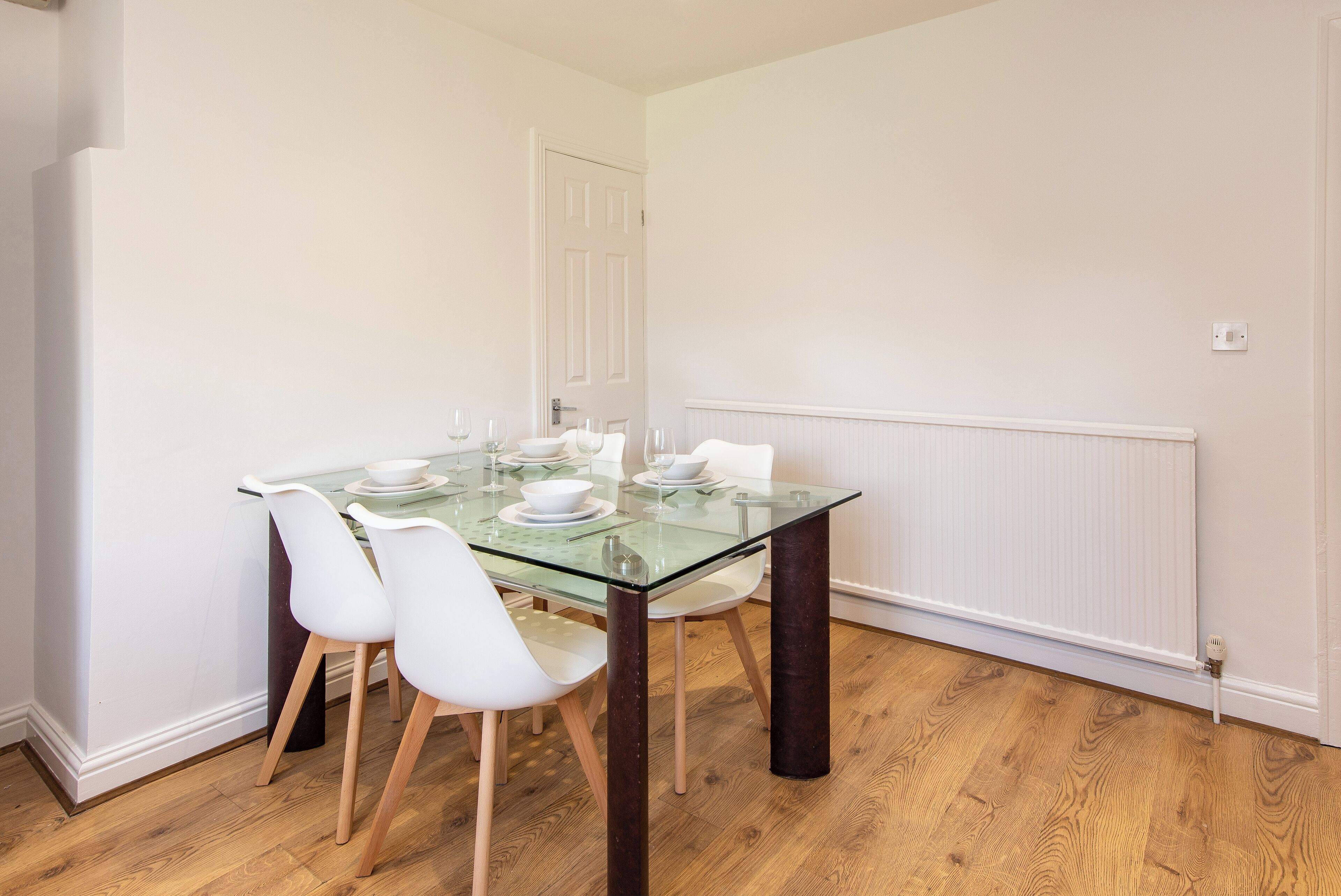 A dining area with a glass table, white chairs, and a white door in the background.