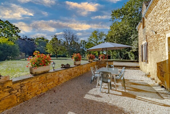 Un patio al aire libre con paredes de piedra, una mesa, sillas y plantas en macetas.