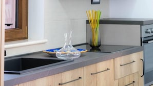 Een keuken met houten kastjes, een zwart aanrecht, een raam met houten kader en een vaas met gele bloemen.