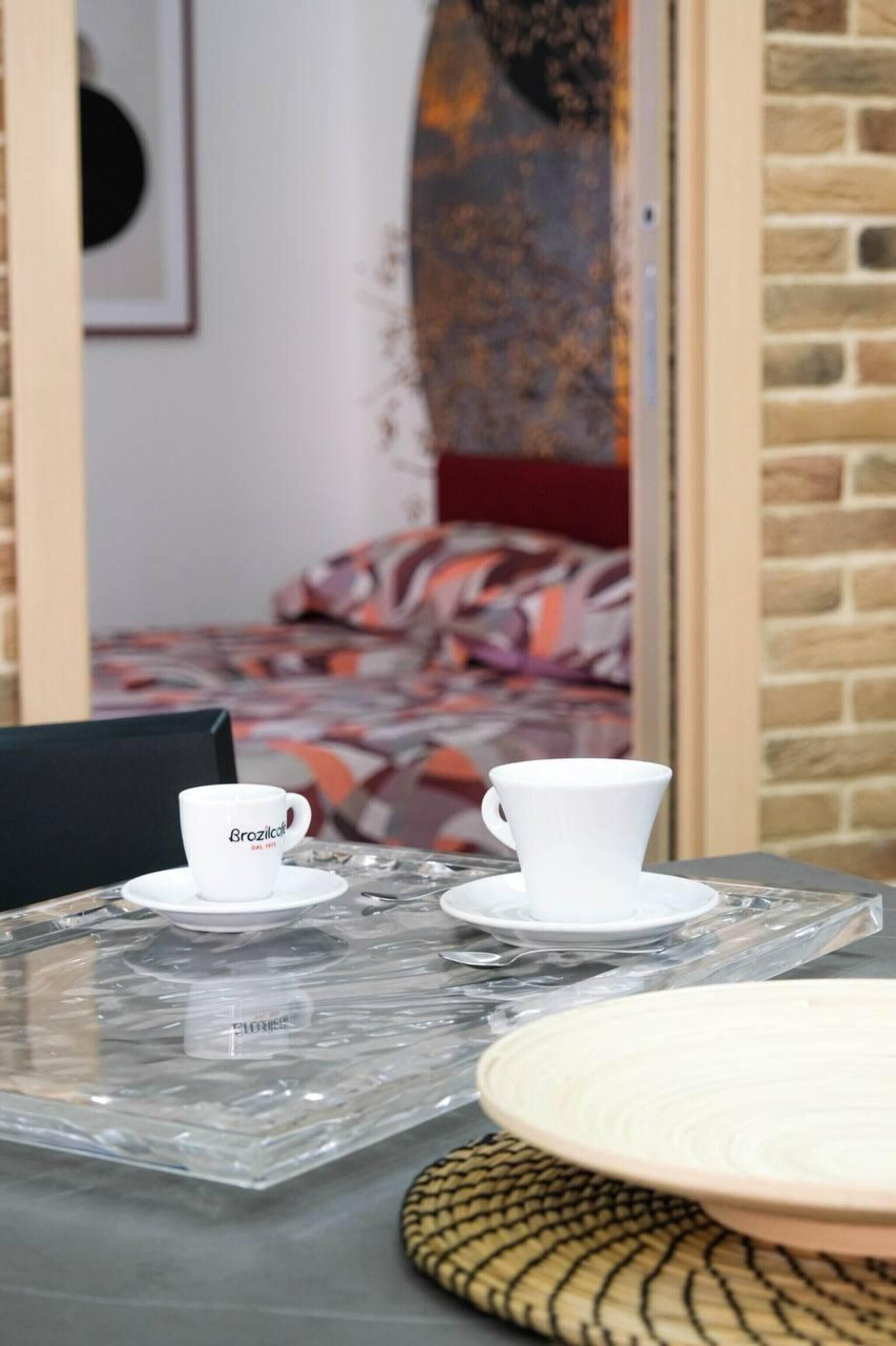 A room with a bed, a coffee table with cups, and a brick wall.