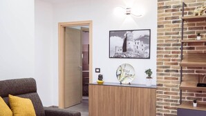 Een moderne woonkamer met een grijze bank, een houten bureau, een wand met baksteenmotief, een ingelijst schilderij en een wandlamp.