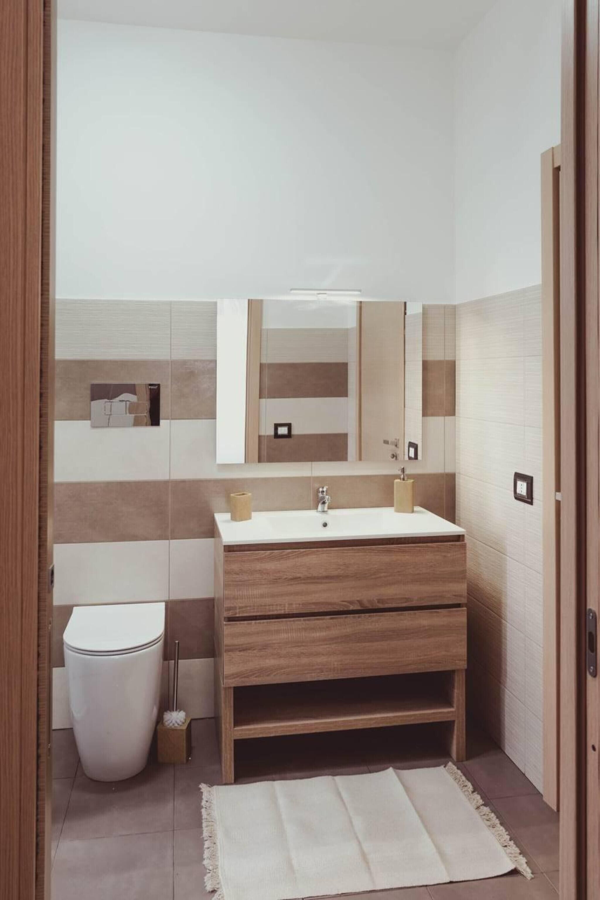 A bathroom with a white sink, wooden vanity, a mirror, and a toilet.