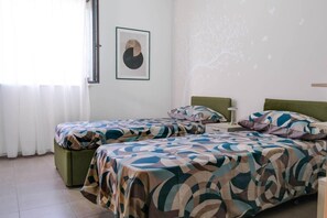 A room with two beds, a window with curtains, a framed picture on the wall, and a tree decal on the wall.