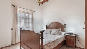 A bedroom with a wooden bed, a nightstand with a lamp, and a window with curtains.