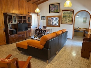 Een woonkamer met een bank, houten kasten, een televisie en een eethoek.