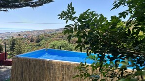 A rectangular pool with a bamboo fence, surrounded by greenery and a view of a hilly landscape.