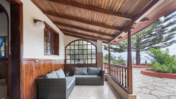 A covered porch with a stone floor, a wicker sofa, and a wooden railing.