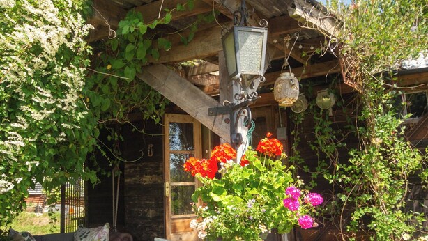 Une cabane en bois rustique, dotée d’un porche, d’une lanterne ancienne et d’un vase à fleurs.
