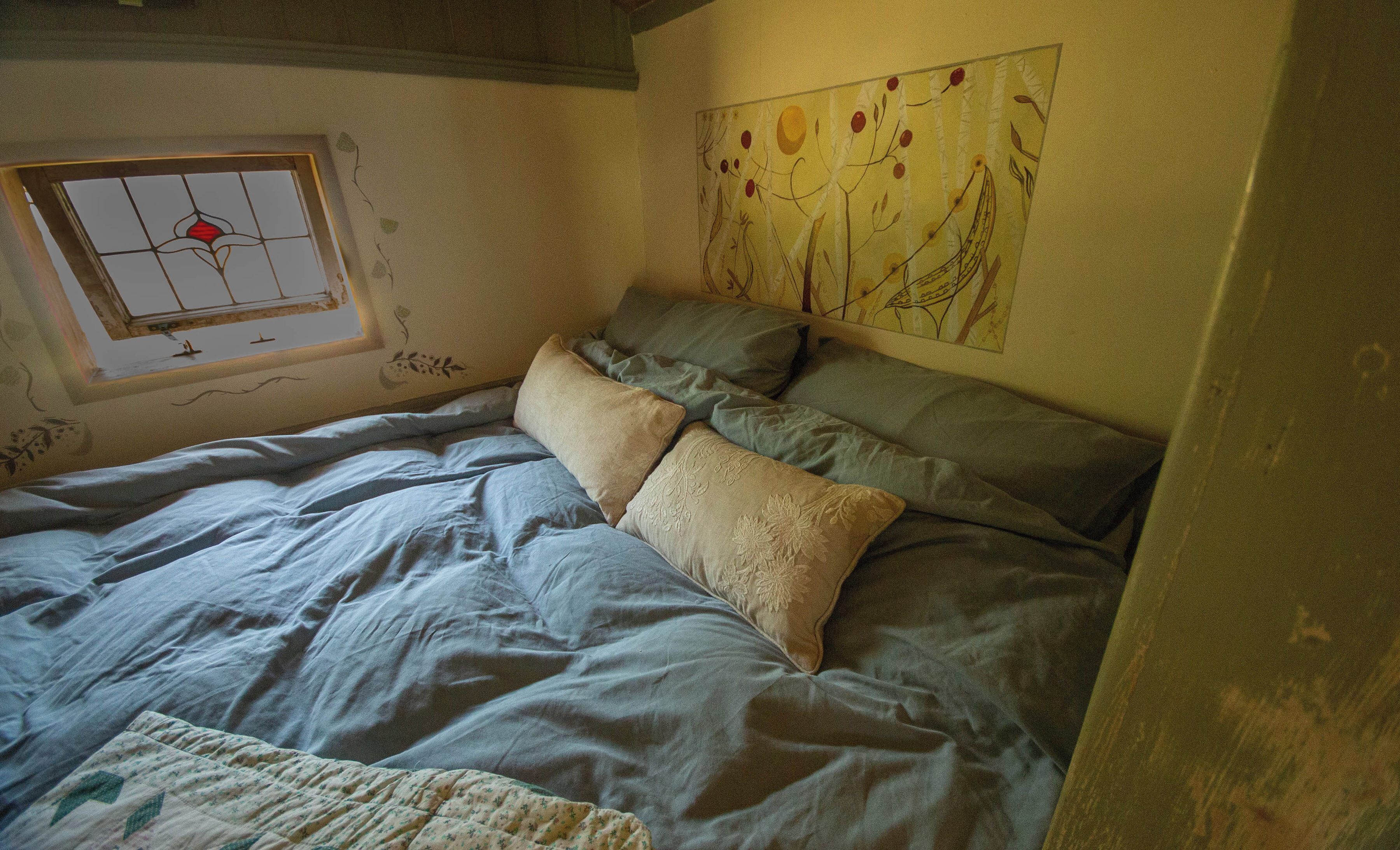 Ein Schlafzimmer mit einem Bett, einem Fenster mit Buntglasdekor und einer Wand mit Blumenbild.