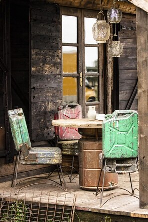 A rustic wooden building with a table and two chairs, a hanging lantern, and a door with a window.