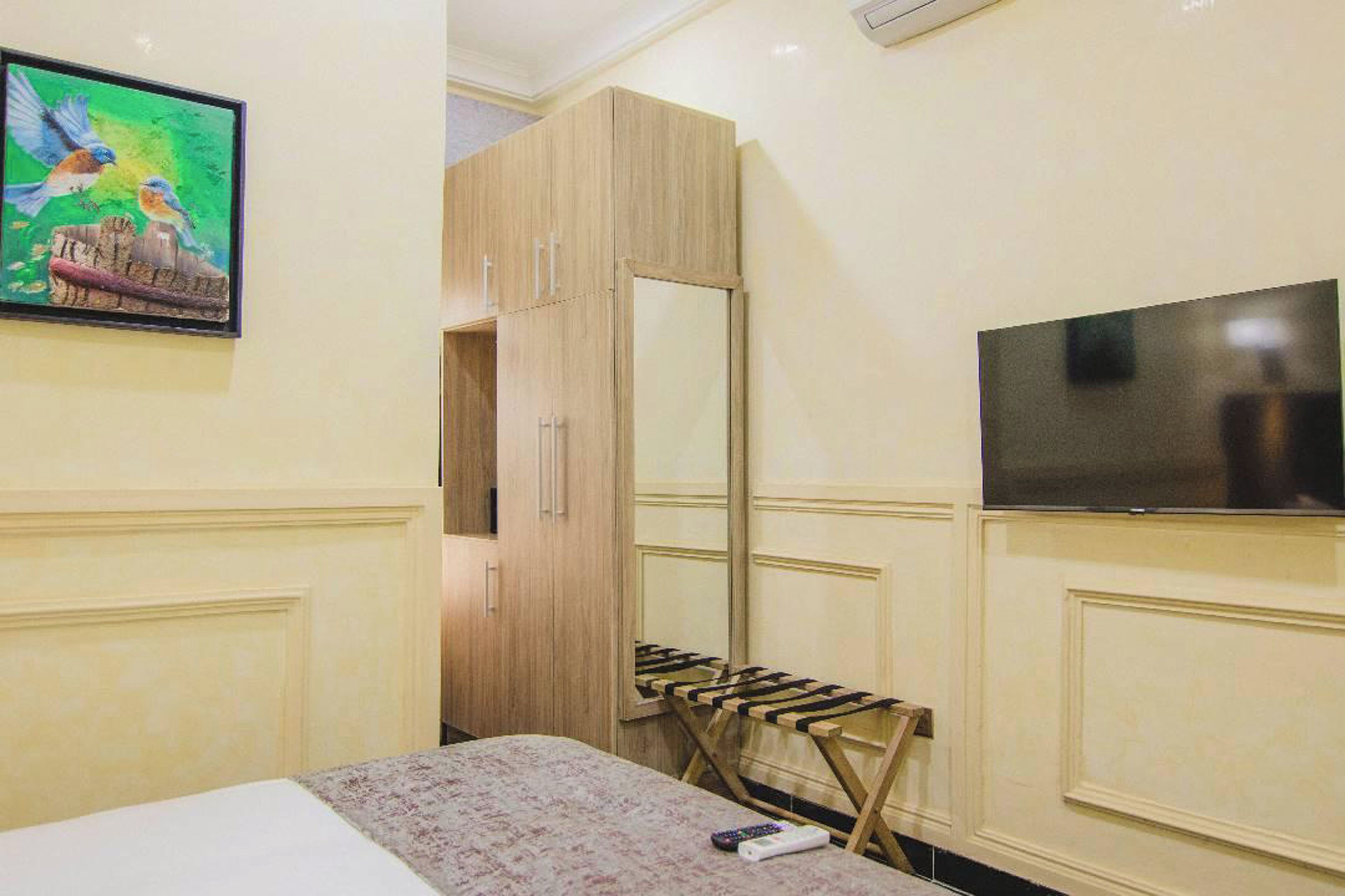 A hotel room with a bed, a wooden wardrobe, a television, and a painting on the wall.