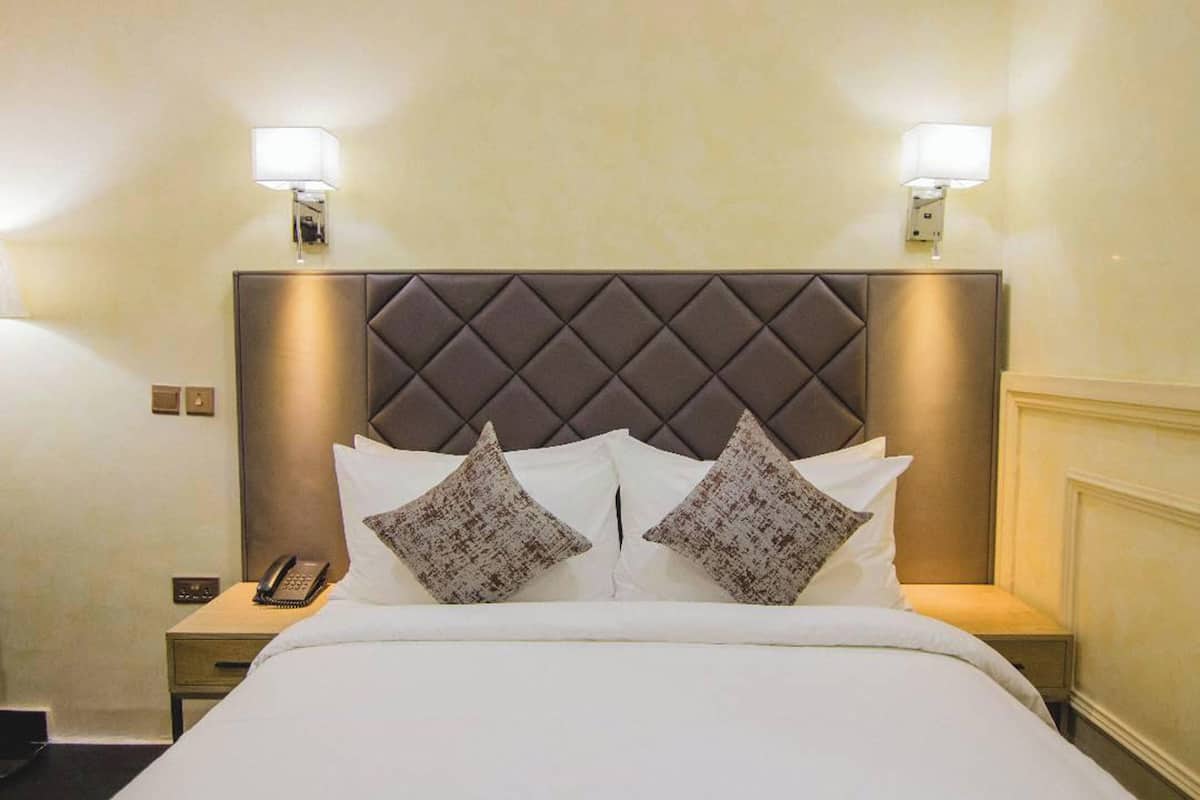 Ein Hotelzimmer mit einem großen Bett, zwei Nachttischlampen, einem Nachttisch mit Telefon und einem gepolsterten Kopfteil.
