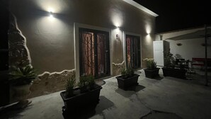 Un bâtiment avec trois fenêtres illuminées et des plantes en pot au premier plan.