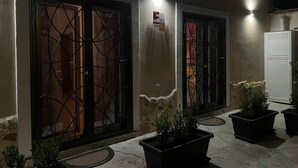 Un bâtiment doté de deux grandes portes richement décorées, avec des grilles en métal, une enseigne au-dessus de l’une des portes, et deux plantes en pot au premier plan.