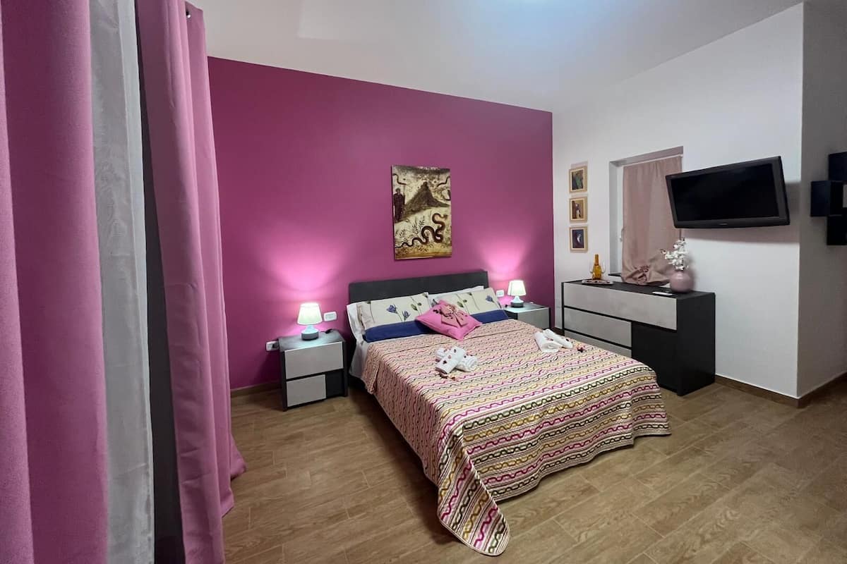 Een slaapkamer met een bed, nachtkastjes, een televisie en een schilderij aan de muur.