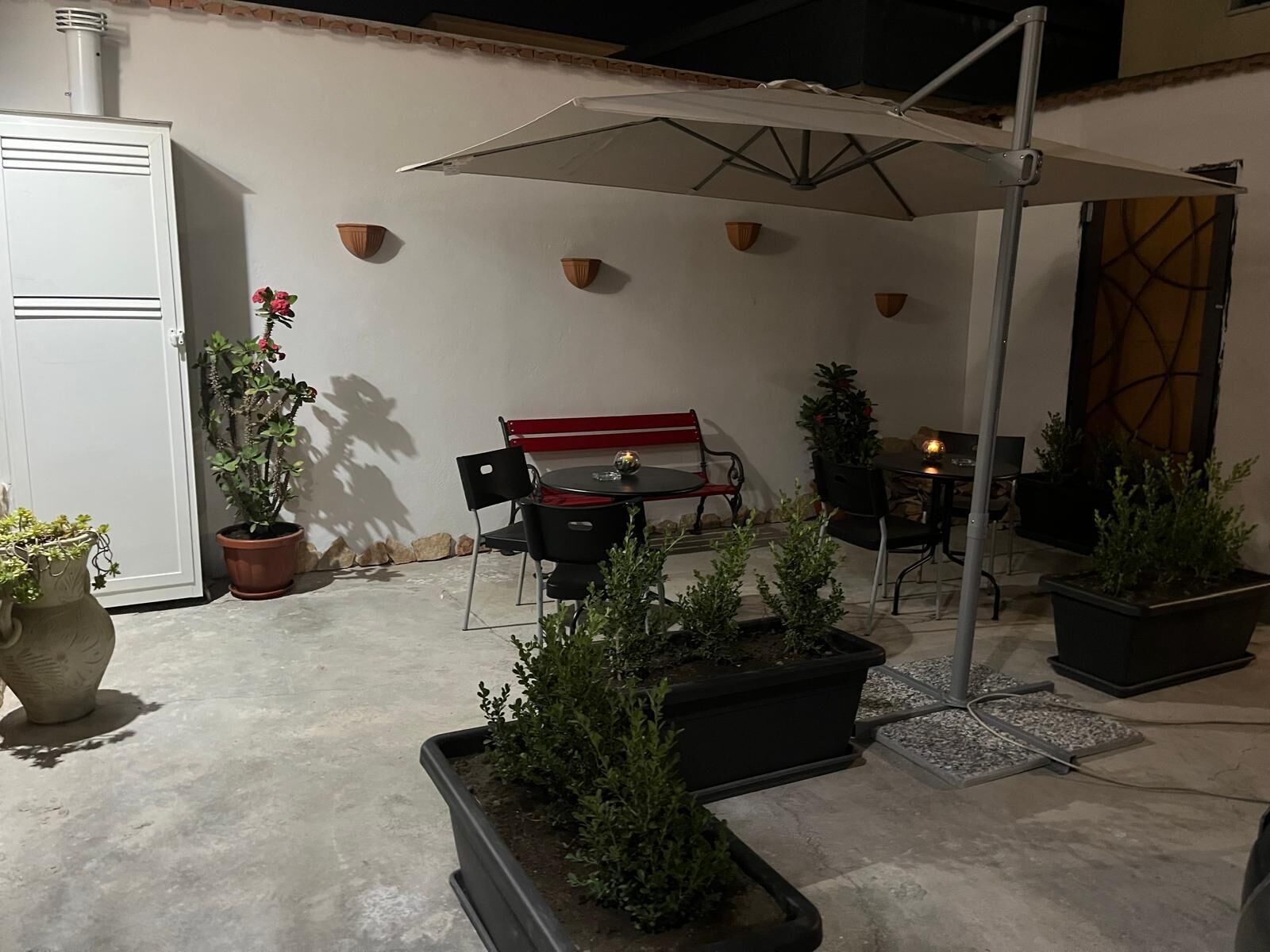 An outdoor patio area with a table and chairs, potted plants, and a white wall with decorative elements.