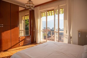 A bedroom with a large bed, wooden wardrobe, and a view of the outside.