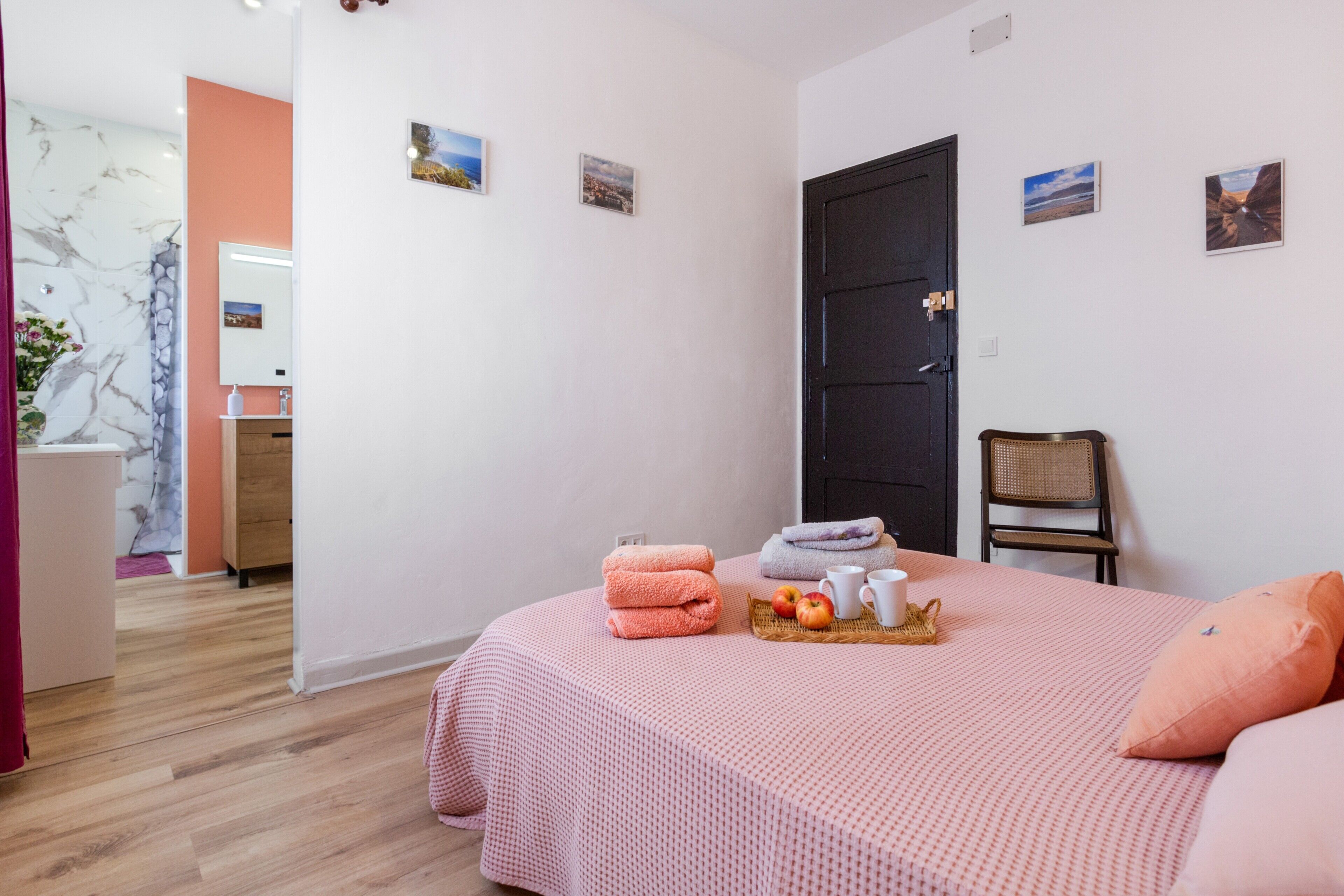 A bedroom with a bed, a chair, a door, and a bathroom visible in the background.