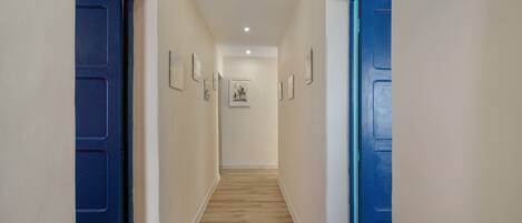 Een gang met houten vloeren, blauwe deuren en ingelijste foto's aan de muur.