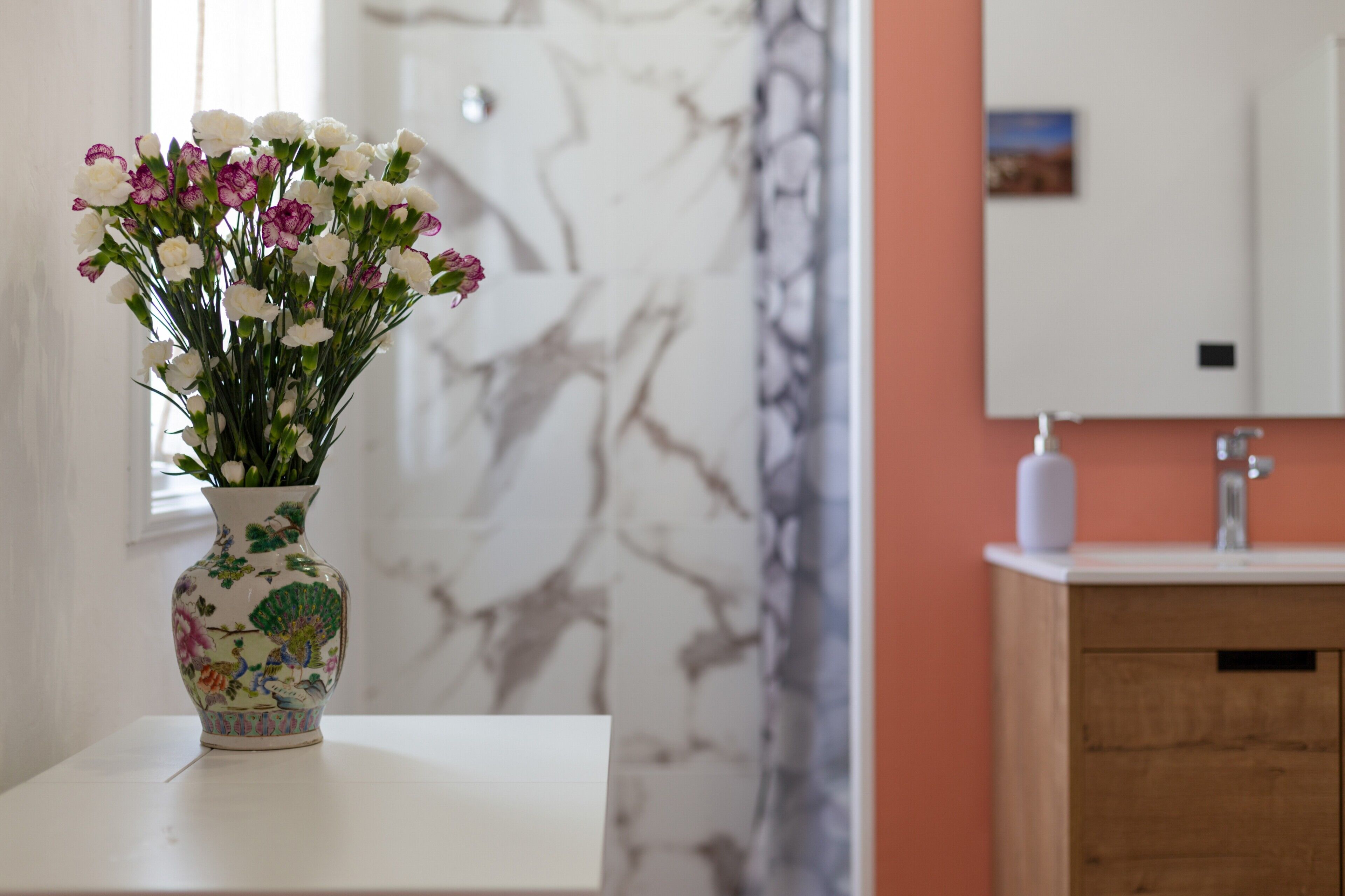A vase with flowers on a white table in a room with a marble wall and a wooden cabinet.