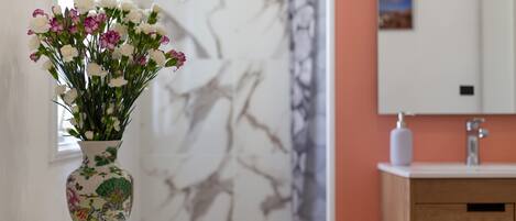 A vase with flowers on a white table in a room with a marble wall and a wooden cabinet.