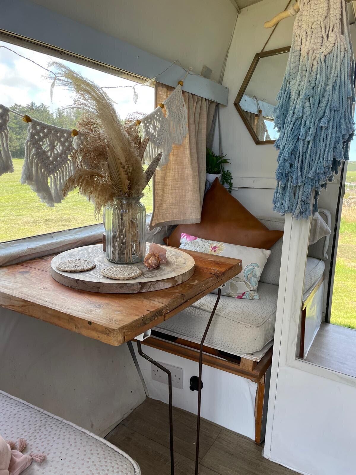 Un interior acogedor con una mesa de madera que sostiene un jarrón decorativo, un banco acolchado con almohadas y un fleco azul colgante.