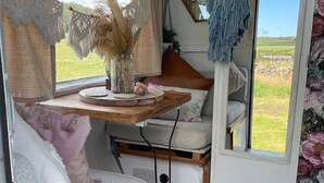 A cozy interior with a wooden table, cushioned seating, and a view of a green field through a window. - Original Vintage Spirit Alpine Caravan Anglesey (Holyhead)