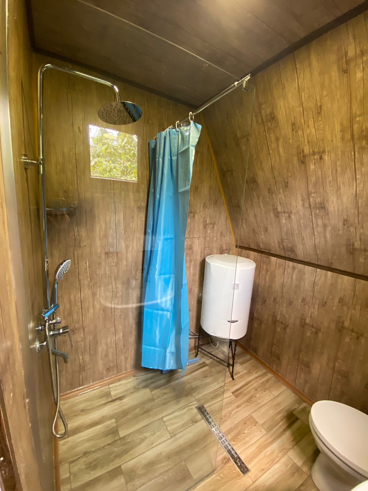 A small, wooden-paneled bathroom with a shower, toilet, and a white water heater.