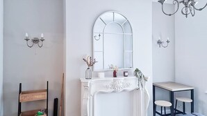Ein modernes Badezimmer mit einem weißen Waschtisch, einem Spiegel mit gebogenem Oberteil, einer Chandelierleuchtre und einem kleinen Tisch mit zwei Hocker.