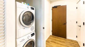 Une buanderie avec des machines à laver superposées et une porte en bois donnant sur une autre pièce.