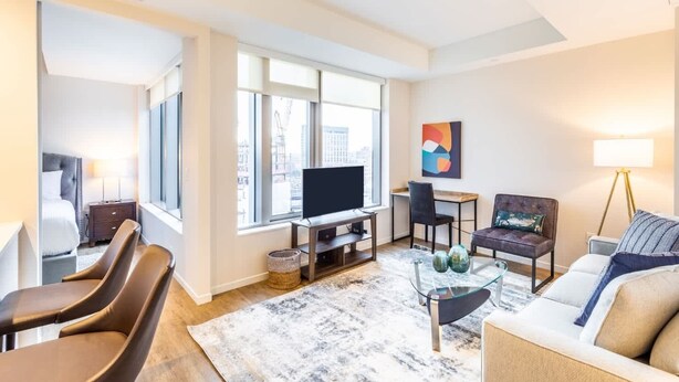 Un salon moderne comprenant un canapé, des fauteuils, un téléviseur et un coin repas.
