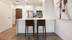 A modern kitchen with white cabinetry, stainless steel appliances, and a central island with two bar stools. - Luxury Apt in Seaport with Gym and Pool (Boston)