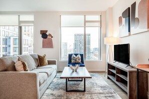 Ein modernes Wohnzimmer mit einer Couch, einem Couchtisch, einem Fernseher und einem großen Fenster mit Blick auf die Stadt.
