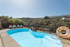 Une piscine à l’eau cristalline, une terrasse en bois et une vue sur un paysage vallonné.