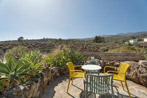 A patio with yellow chairs and a table, surrounded by rocks and plants, overlooking a hilly landscape. - "Casa Rural La Venta" with Sea View, Private Pool & Wi-Fi (Las Vegas)