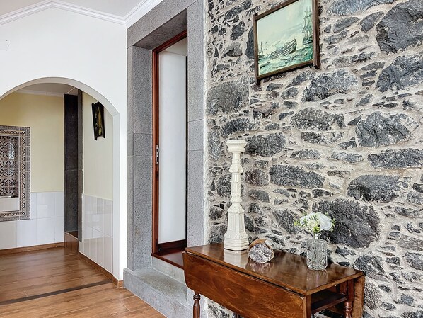 A hallway with a stone wall, a wooden table with a vase and flowers, and a framed picture on the wall.