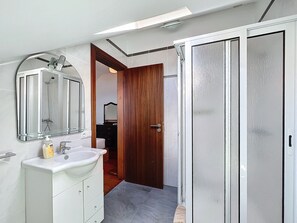 A bathroom with a white sink, mirror, and shower. There is a wooden door leading to another room.