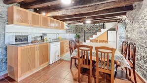 Een rustieke keuken met houten kastjes, een witte vaatwasser en een eethoek met een tafel en stoelen.