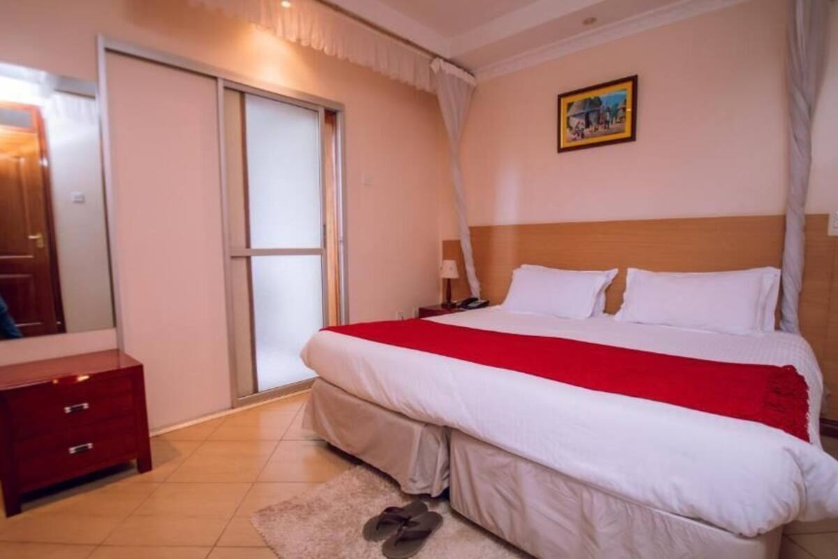 A bedroom with a bed, a nightstand, a dresser, a door, and a painting on the wall.