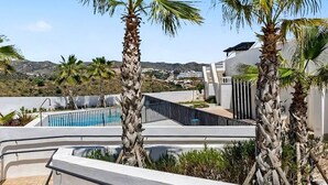 A rooftop pool area with palm trees, a clear sky, and a view of distant hills.