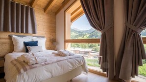 A bedroom with a large window, wooden walls, and a bed with white bedding. - Praz-sur-Arly | Sleeps 6 | Vues imprenables (Praz-sur-Arly)
