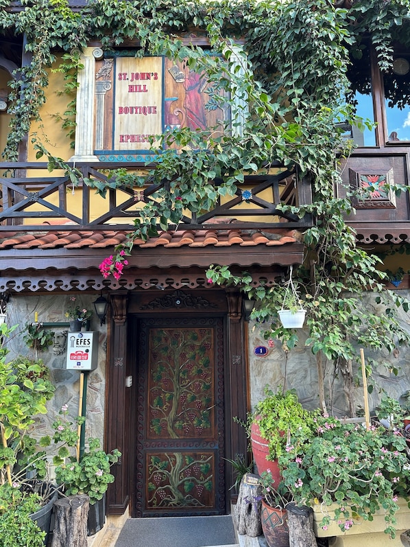A traditional building with a wooden sign for St. John's Hill Boutique, a stone wall, and a door with a grapevine design. - St.Johns hill boutique Ephesus (Selçuk)