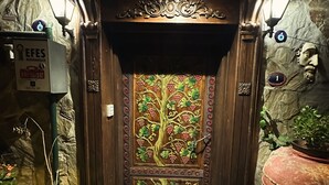 Een houten deur met een ontwerp van een boom en fruit, een brievenbus, en een grote plantenbak met groen.