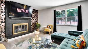 Ein Wohnzimmer mit Kamin, einer Couch, einem Couchtisch und einem Fernseher, der 'NETFLIX' anzeigt.