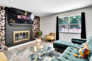 A living room with a fireplace, a sofa, a coffee table, and a TV displaying 'NETFLIX'.