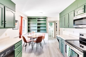 A modern kitchen with green cabinets, a dining table with chairs, and a built-in oven.