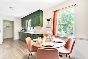 A dining area with a round table set for four, green cabinets, and a window with curtains.